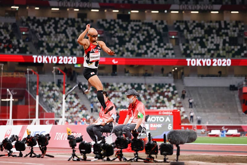 山本篤選手が走り幅跳びで空中で飛んでいる。